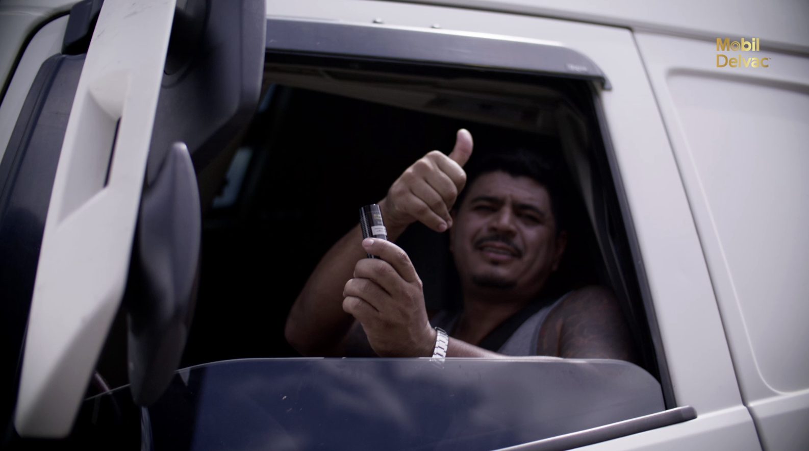Truck driver giving a thumbs up while holding the Mobil Delvac sunscreen from his cab window