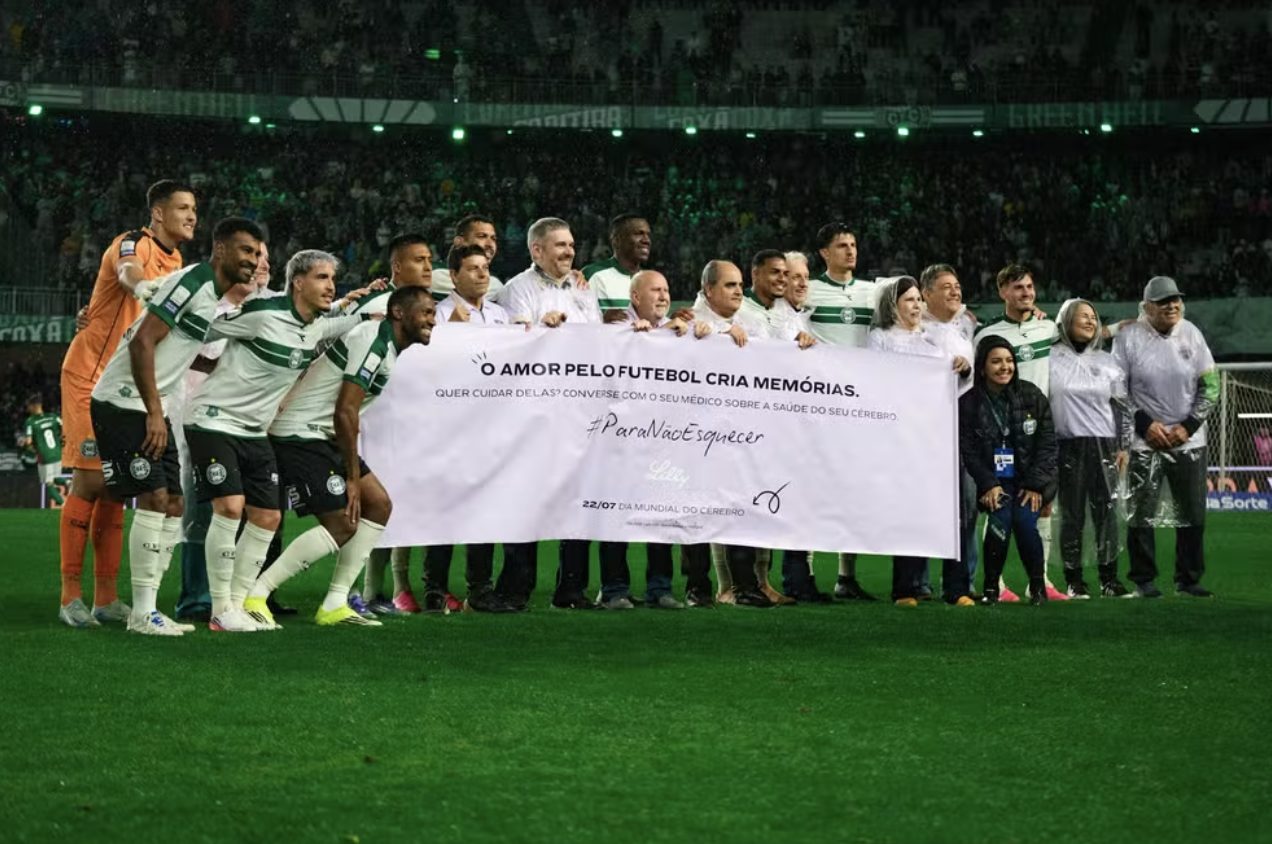Coritiba players and elderly fans holding the #ParaNaoEsquecer banner on the pitch at Couto Pereira