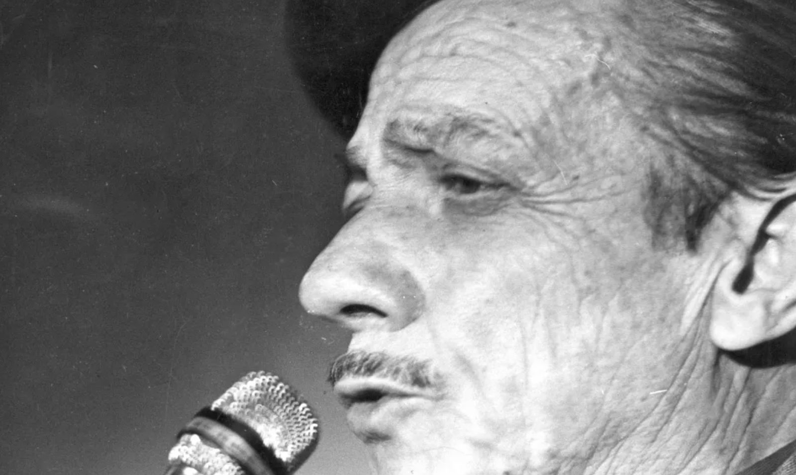 Black and white portrait of Adoniran Barbosa singing into a microphone